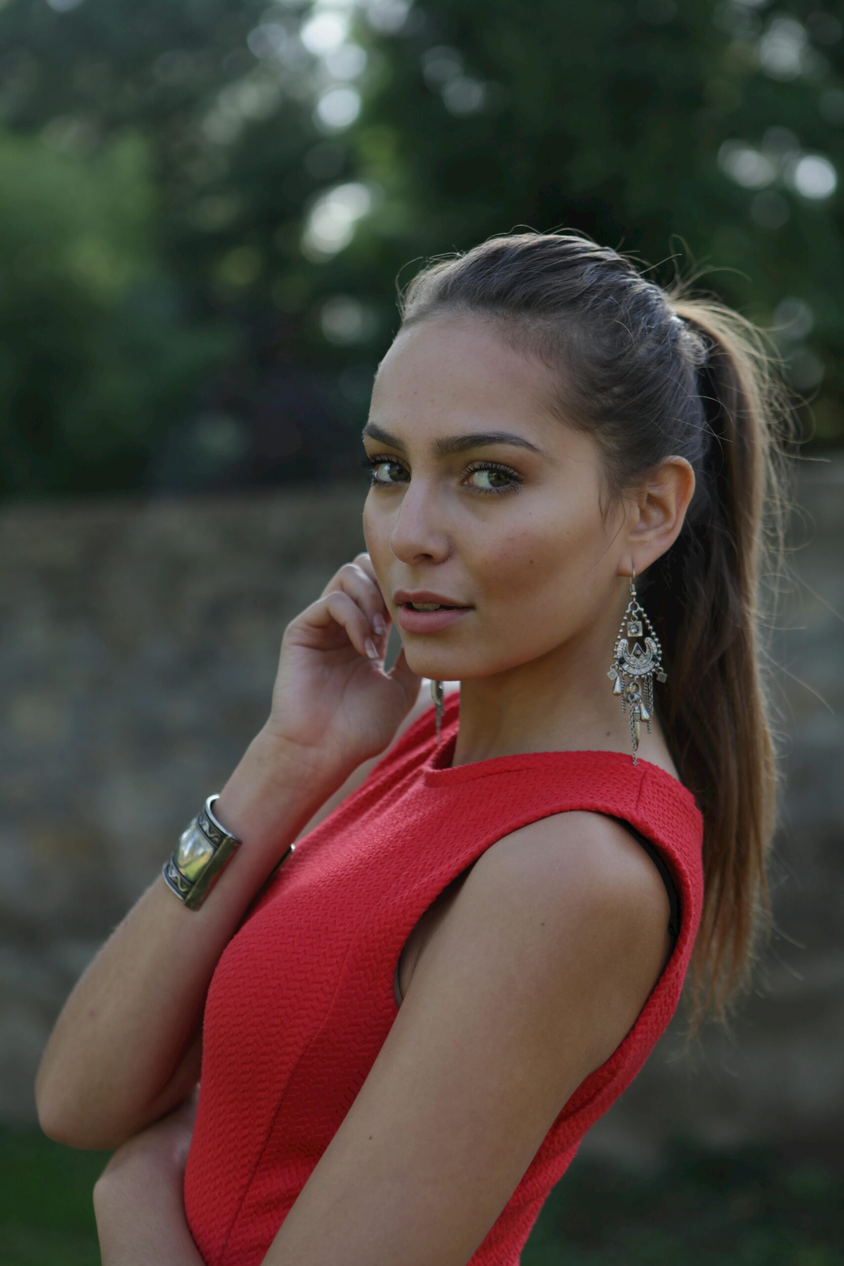 About Chic beauty in a red dress, posing gracefully outdoors with statement jewelry.